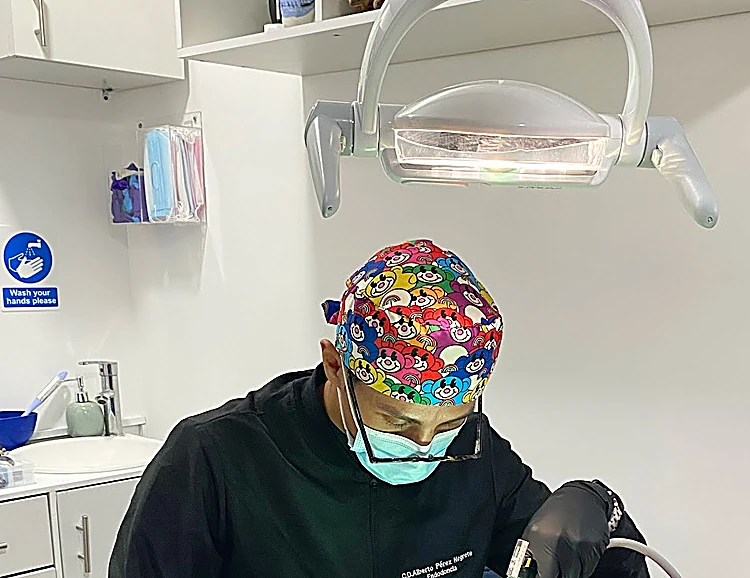 Especialista del consultorio con gorro quirúrgico de colores y cubrebocas, trabajando bajo la lámpara dental